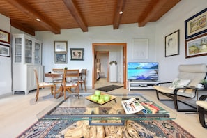A living room with a wooden ceiling, a dining area with a cabinet, a television, and a sofa.