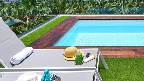 A poolside area with a view of the ocean, a wooden deck, and lounge chairs.