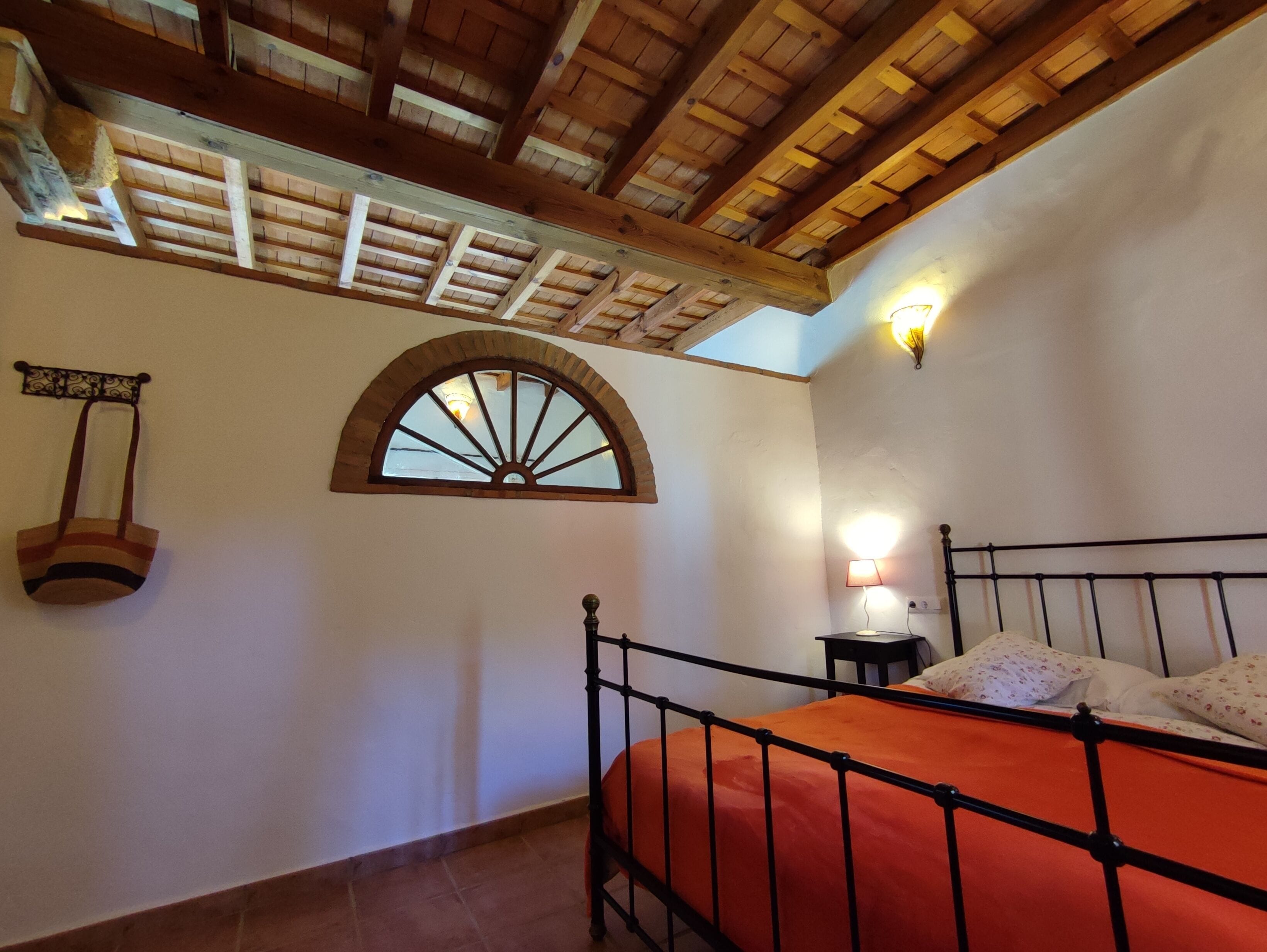 Un dormitorio con cama, mesita de noche, lámpara, ventana y estante fijado a la pared.