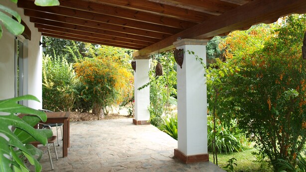 Ein überdachter Patio-Bereich mit Steinböden, Holzbalken und weißen Säulen.