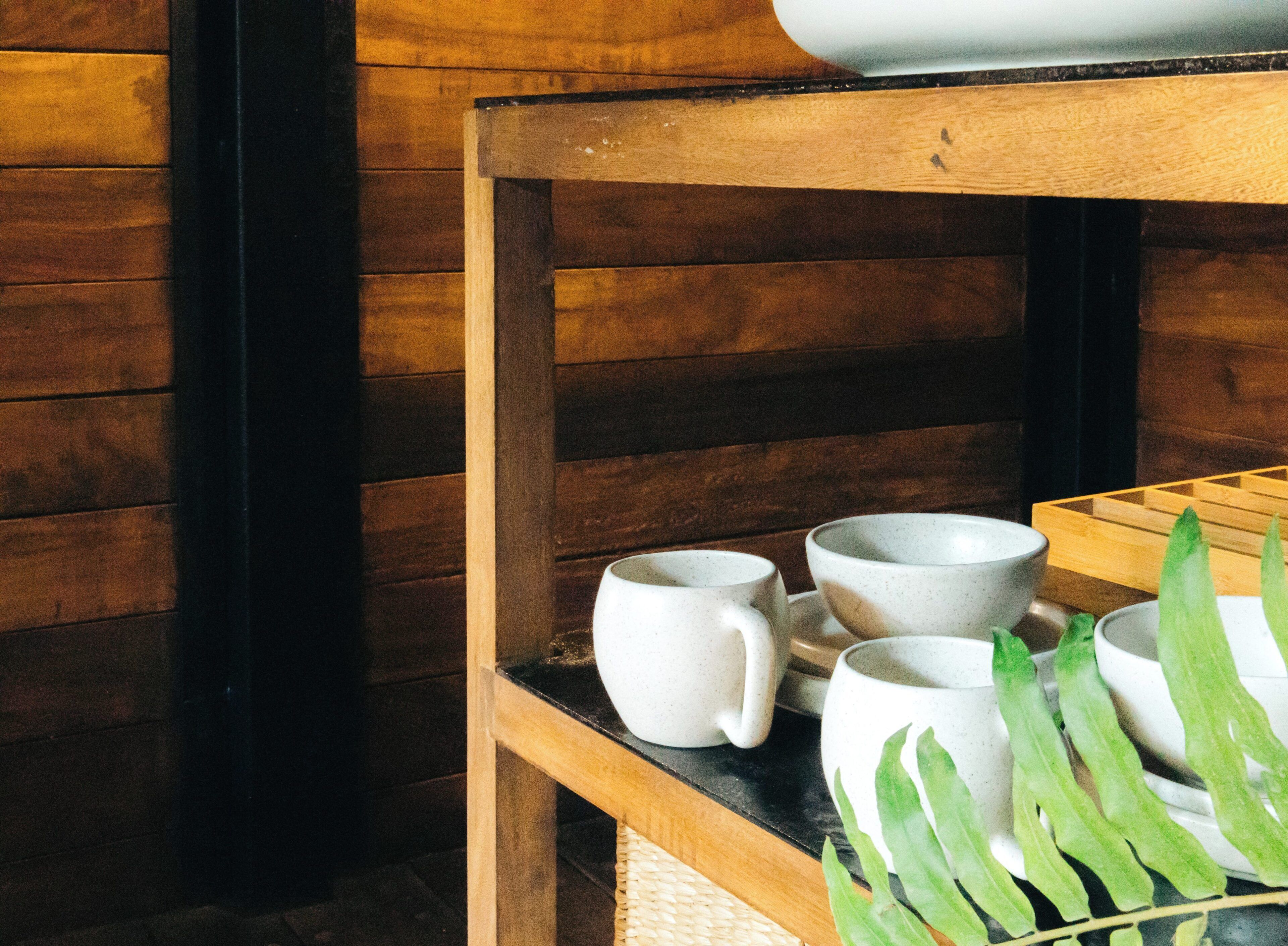 Una silla de madera con un estante que sostiene tazas y platillos de cerámica blanca.