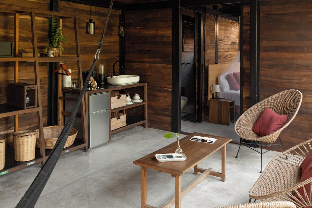 Un interior moderno con techo de madera, zona de cocina y mobiliario de mimbre.
