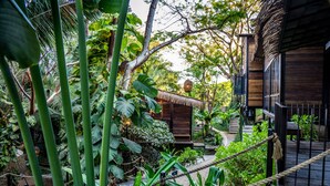 A lush garden with a wooden building, rope barriers, and a thatched-roof structure.