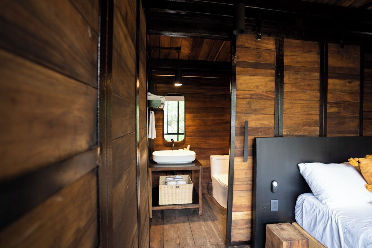 A wooden cabin-style room with a bed, a white sink, and a window.