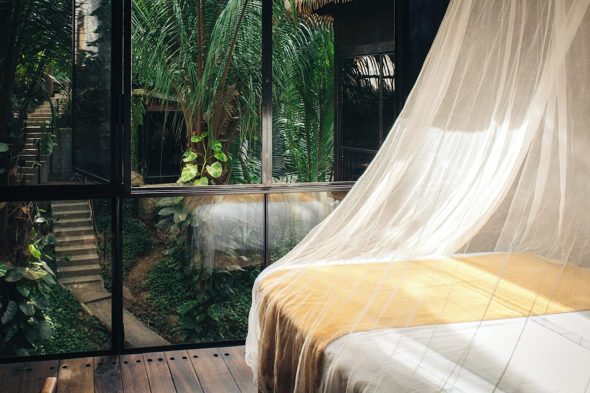 Un dormitorio con cama, ventana y vista a un jardín.