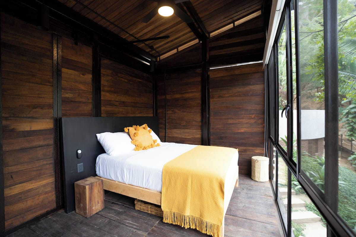 Una habitación de madera con una cama, un ventanal y un ventilador de techo.