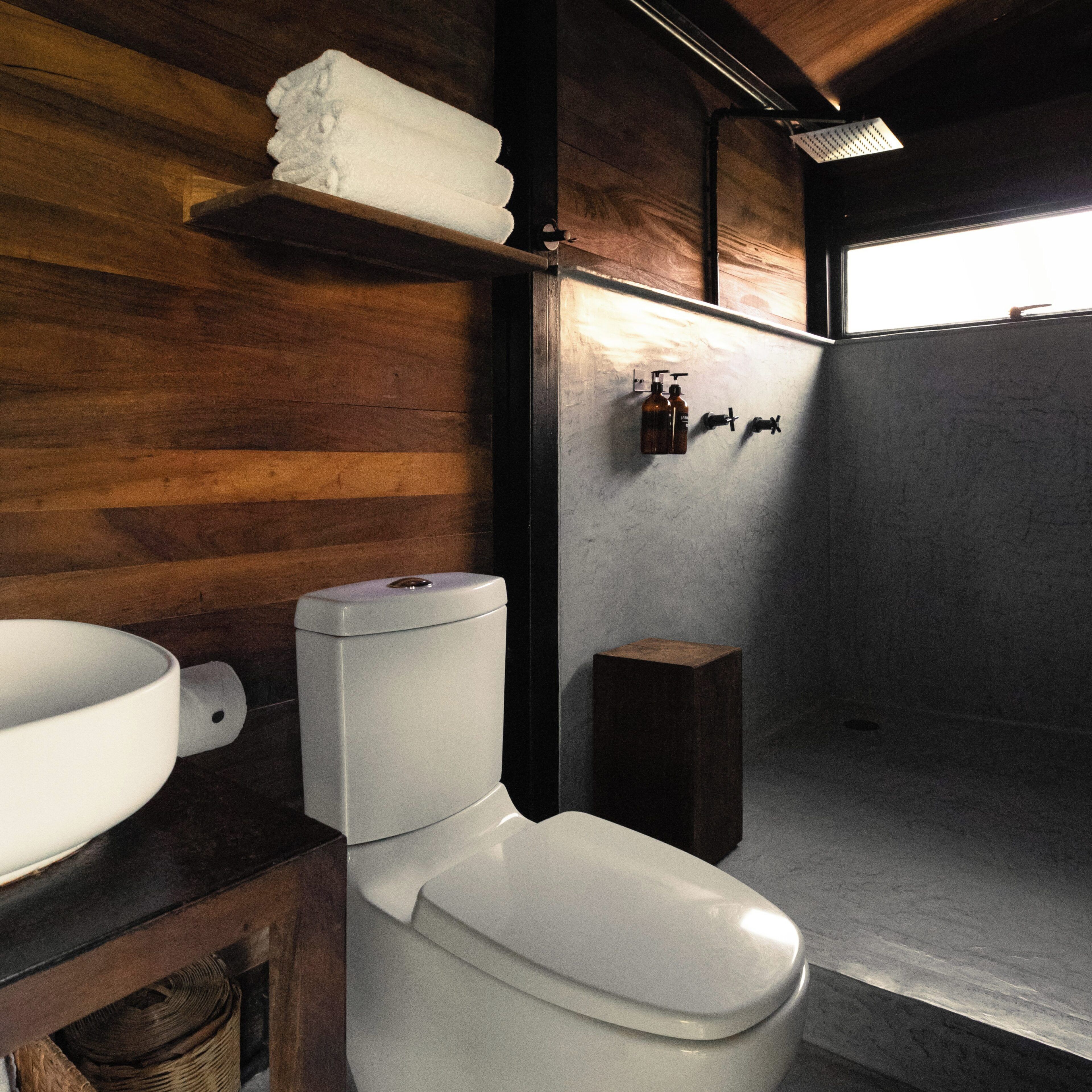 Une salle de bain moderne avec un meuble-lavabo en bois, des toilettes blanches, un grand lavabo et un espace douche.