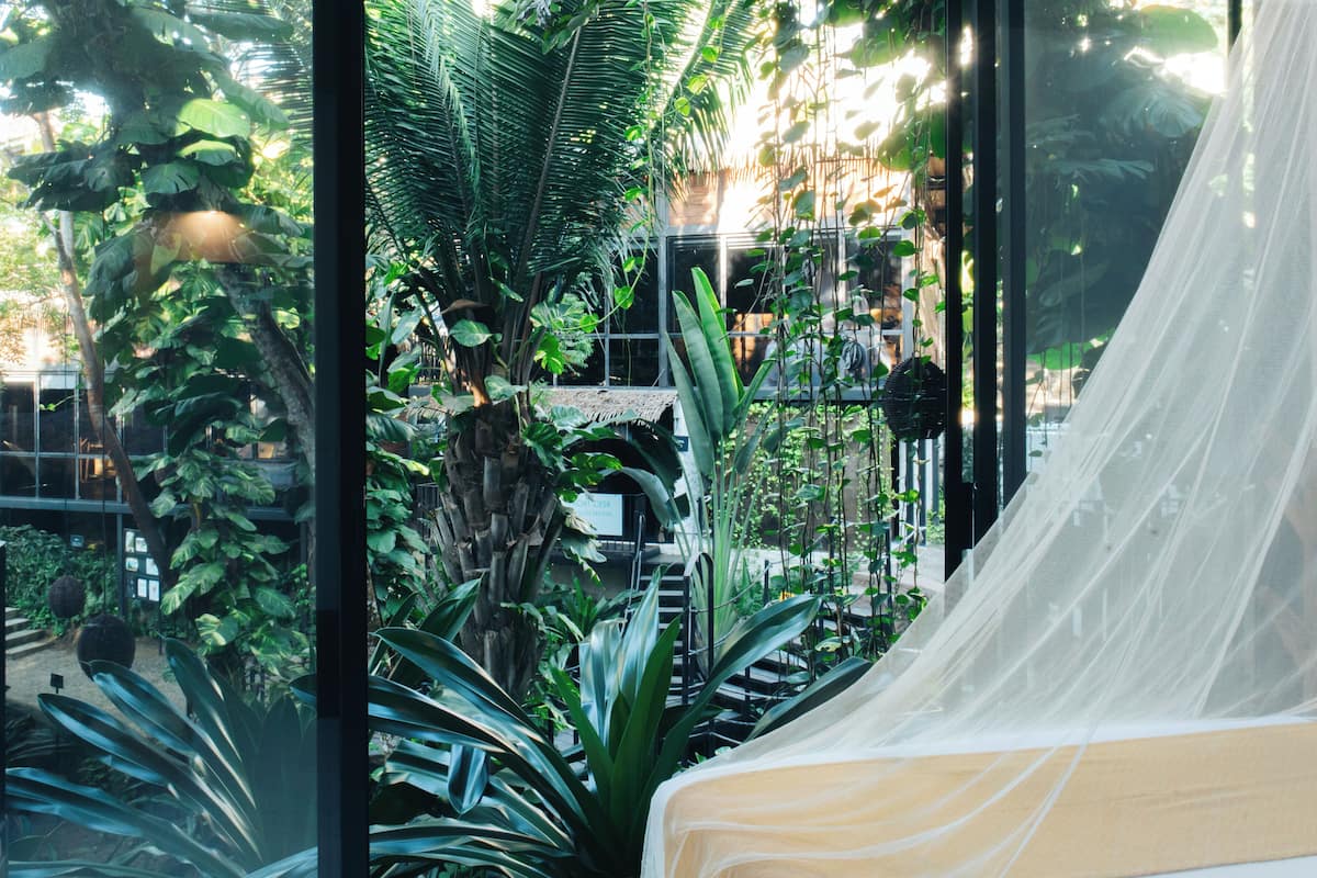 Una habitación con cama, ventana y vistas a un jardín con diversas plantas.