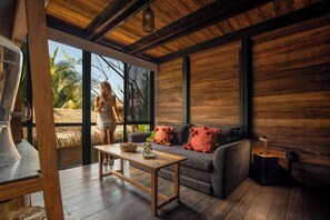 Una habitación con piso de madera, un sofá con cojines rojos, una mesa de madera y un ventanal con vista a palmeras.