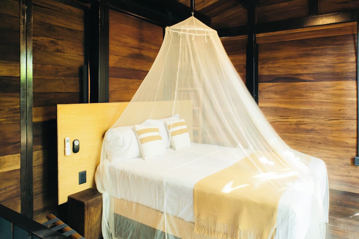 Una cama con dosel, paredes de madera, una mesita de noche y un interruptor de luz en la pared.