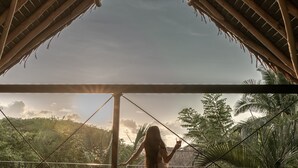 A person standing under a wooden roof structure, overlooking a garden with tropical plants.
