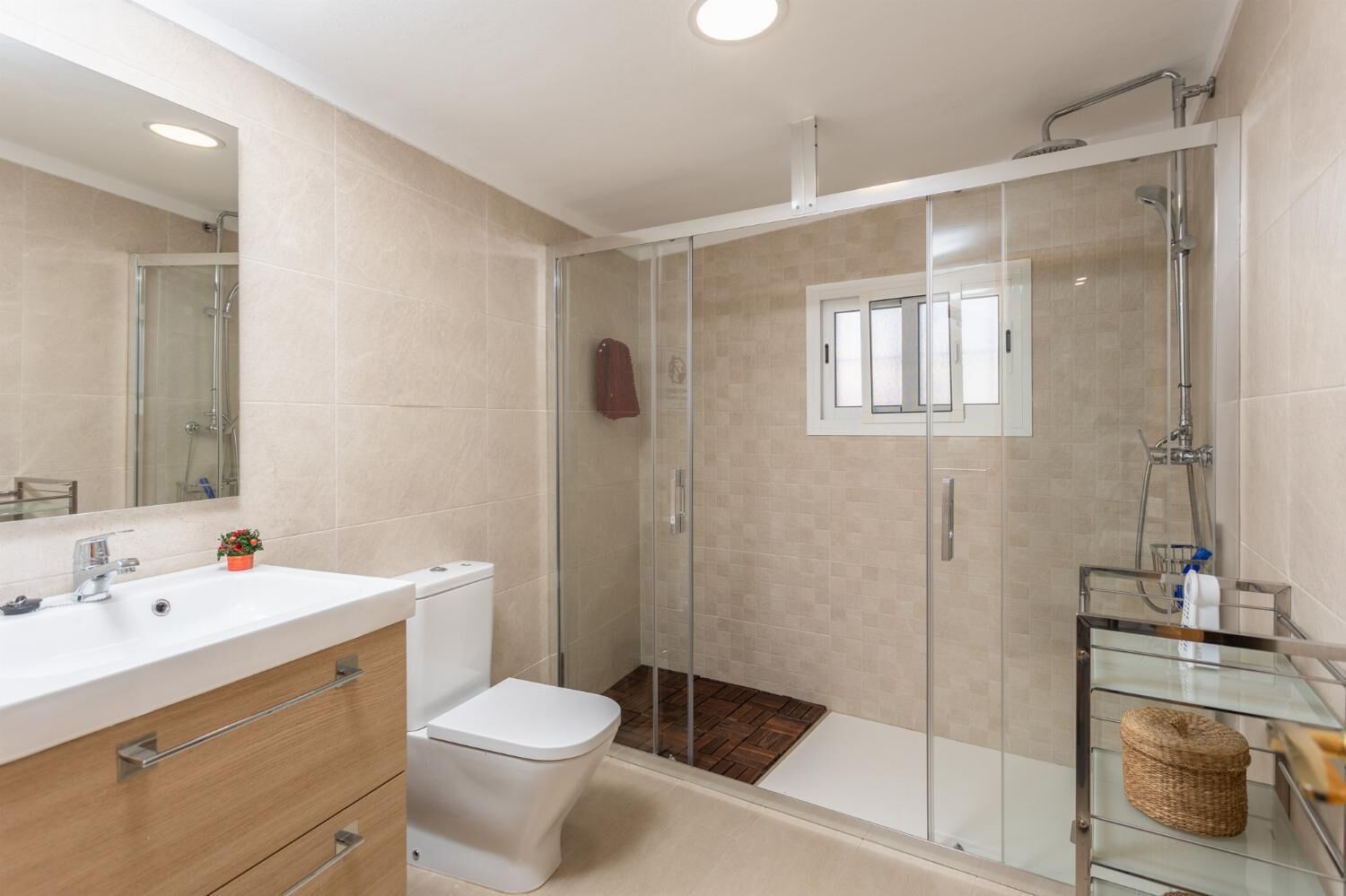 Een moderne badkamer met een glazen douchecabine, een wit wastafelmeubel en een toilet.