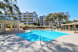 Uma piscina com espreguiçadeiras e um gazebo, cercada por edifícios altos.