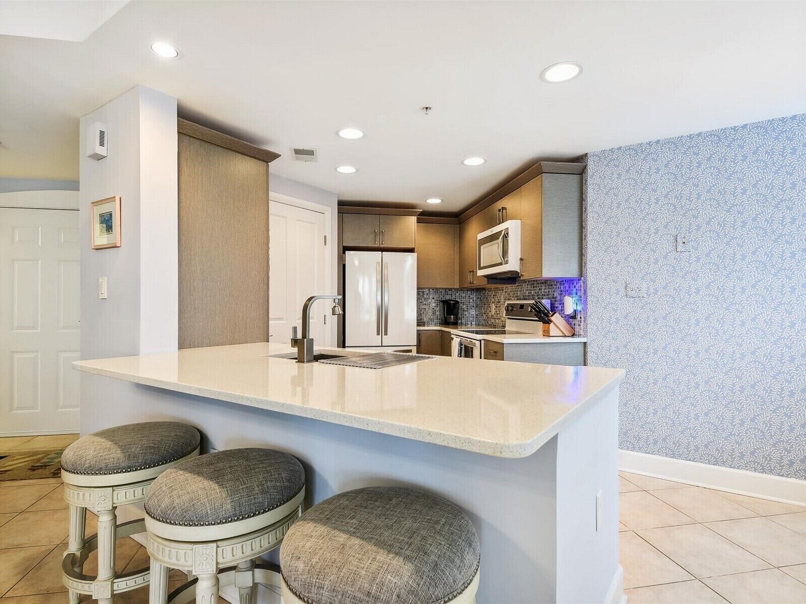 A modern kitchen with a central island, bar stools, stainless steel appliances, and a patterned backsplash.