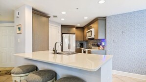 Una cocina moderna con una isla central, taburetes de bar, electrodomésticos de acero inoxidable y un salpicadero decorativo.