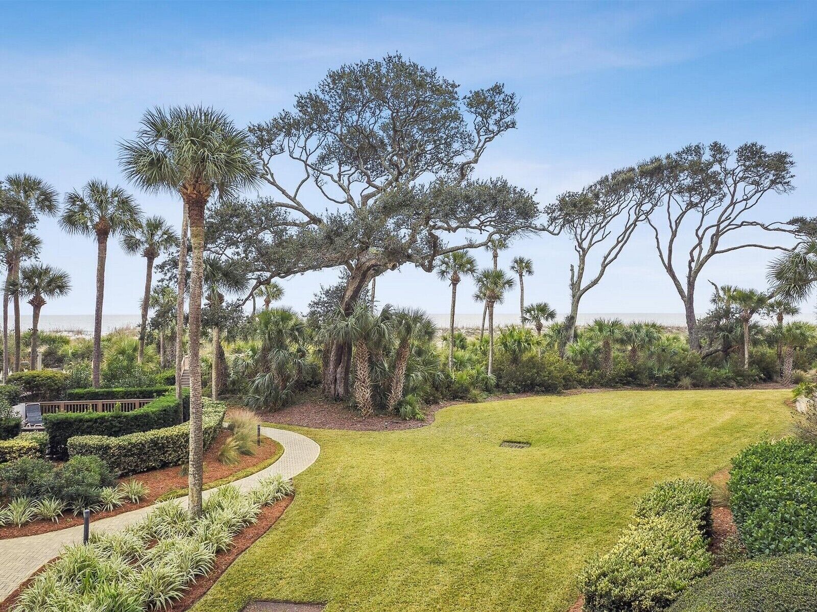 A well-maintained garden with a variety of trees, a curved pathway, and a grassy lawn.
