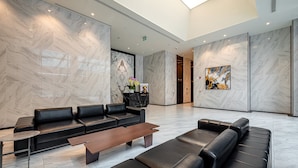 Un hall d’entrée moderne avec des canapés en cuir noir, une table basse en bois, des murs en marbre et une œuvre d’art encadrée.