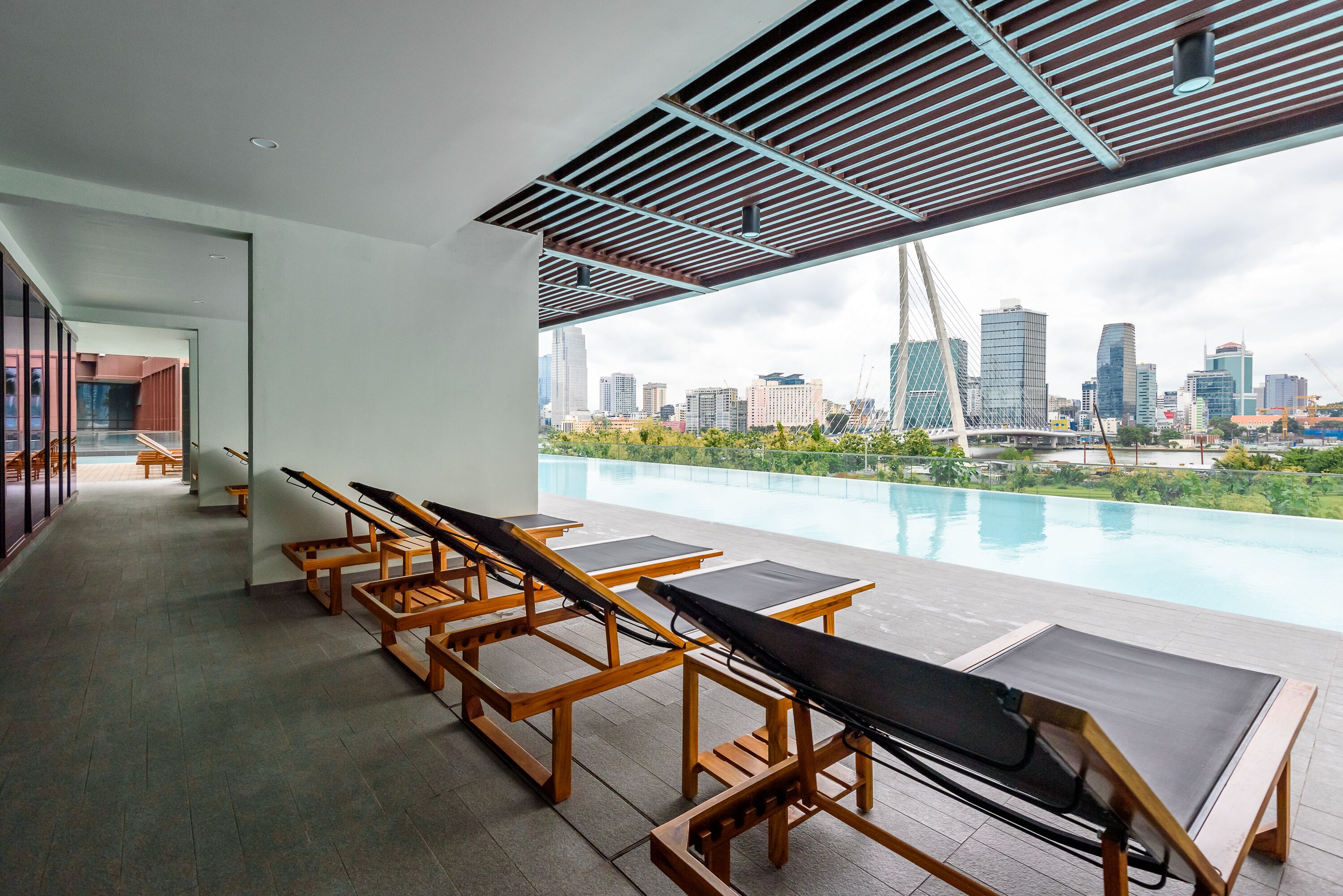 A modern hotel room with a city view, a pool, and sun loungers.