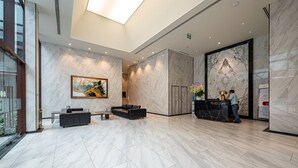 Un hall d’entrée moderne avec un sol en marbre, un comptoir d’accueil, un canapé et un grand tableau abstrait.