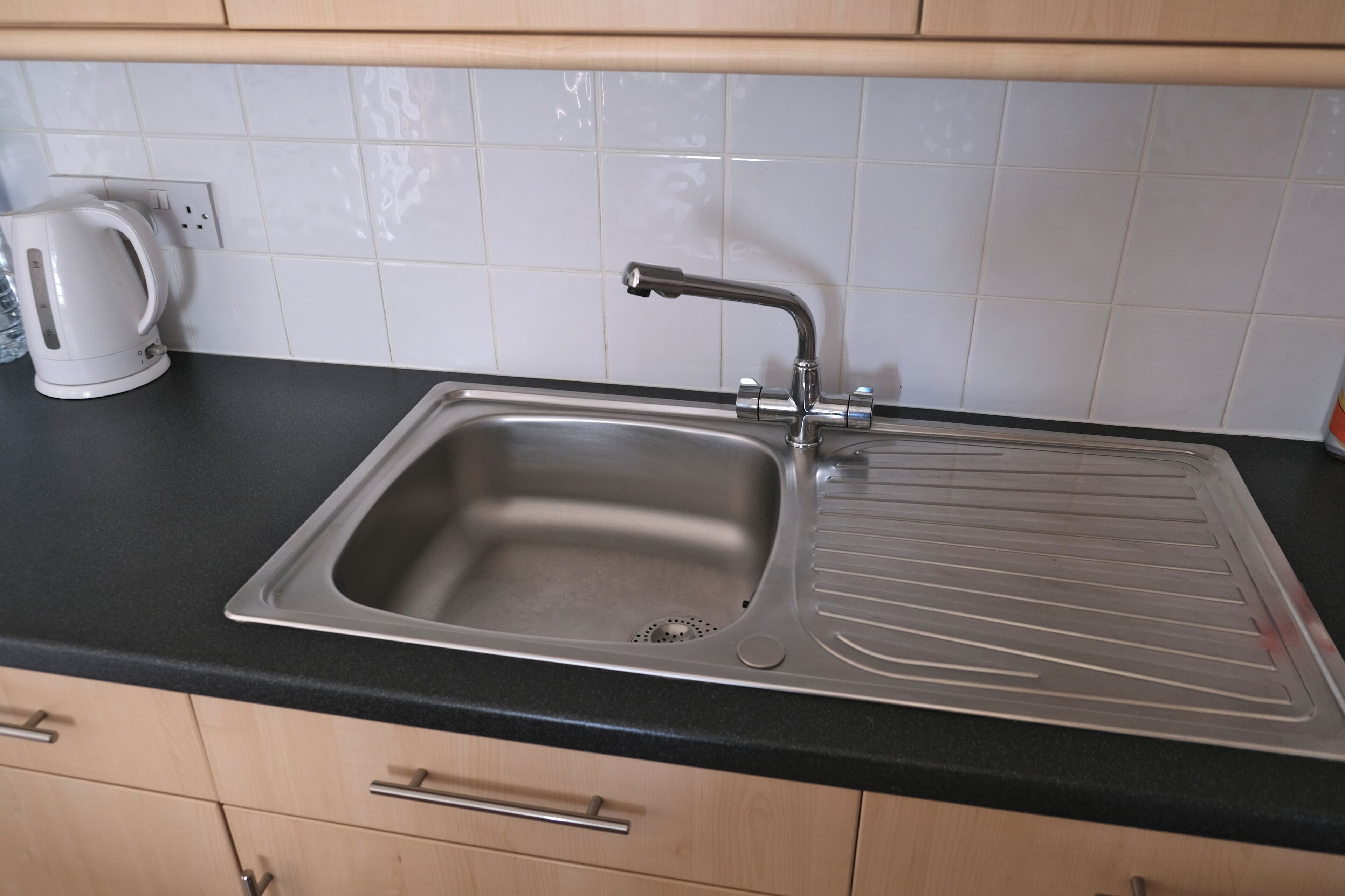 Cucina con lavello in acciaio inox, bollitore e pensili in legno.