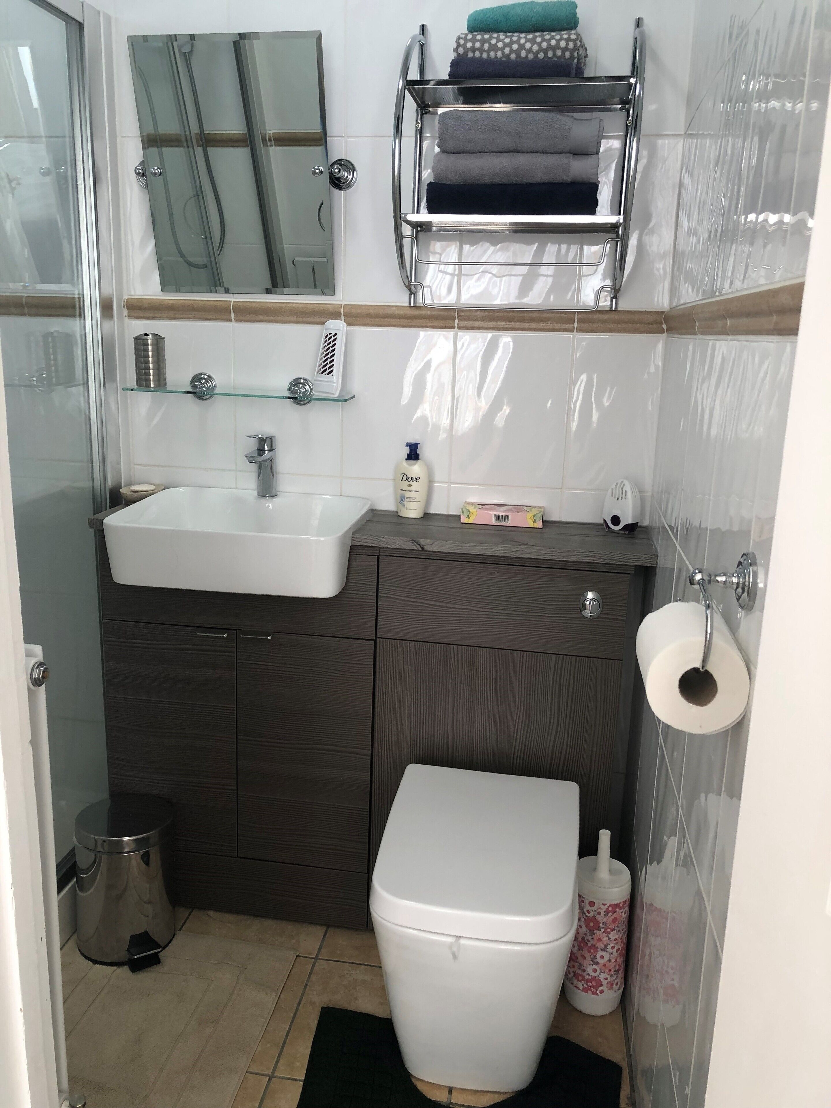 Une salle de bain moderne avec un lavabo blanc, un meuble-lavabo en bois foncé, une cabine de douche en verre et des toilettes dotées d’un porte-serviettes en papier.