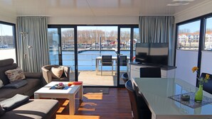 A modern living room with a sofa, coffee table, and a TV on a glass table. - Hausboot in Boltenhagen (Boltenhagen)