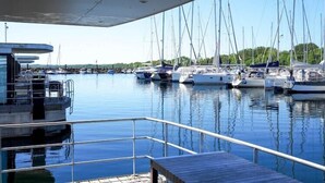 Un port de plaisance où sont amarrés de nombreux bateaux, une zone abritée avec une rambarde et une vue dégagée sur l’eau et la côte lointaine.
