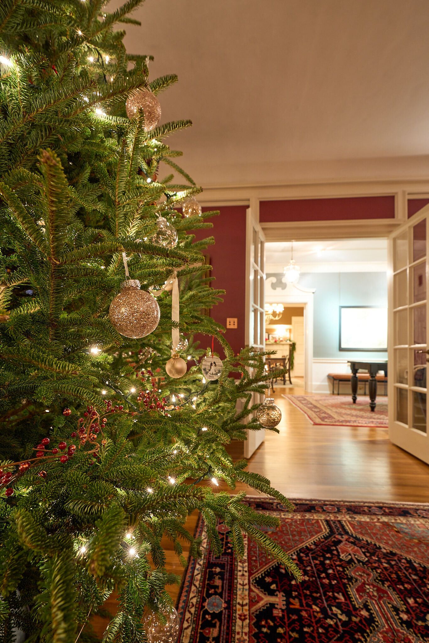 Un árbol de Navidad con luces y adornos en una habitación con piso de madera y alfombra estampada.