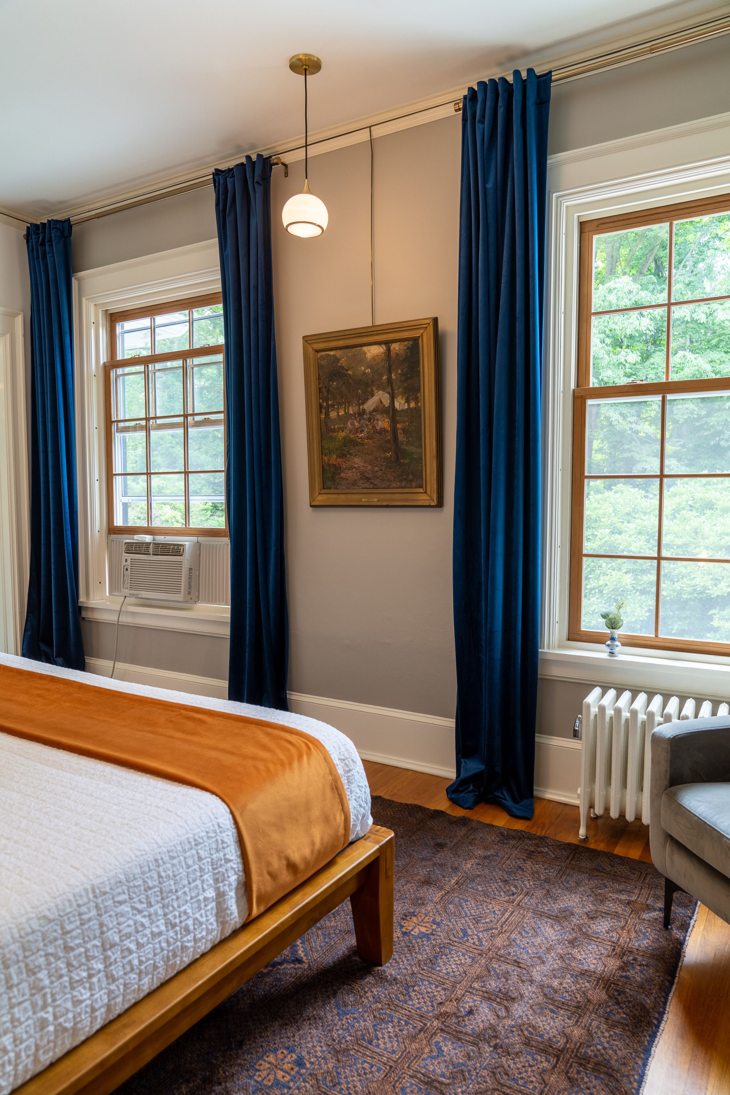 A bedroom with a bed, a radiator, a window with curtains, and a painting on the wall.