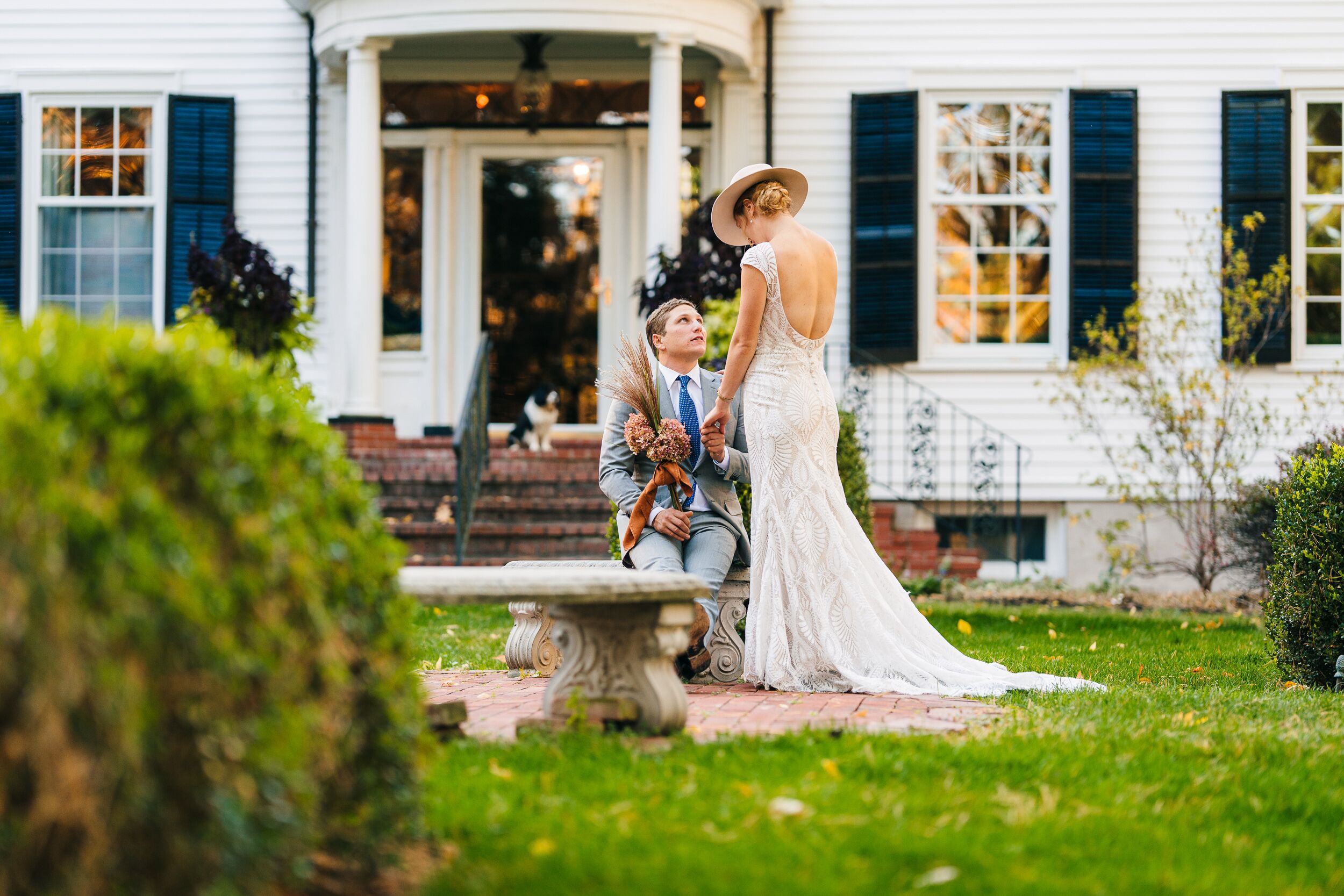 A couple in a garden setting with a white building in the background.