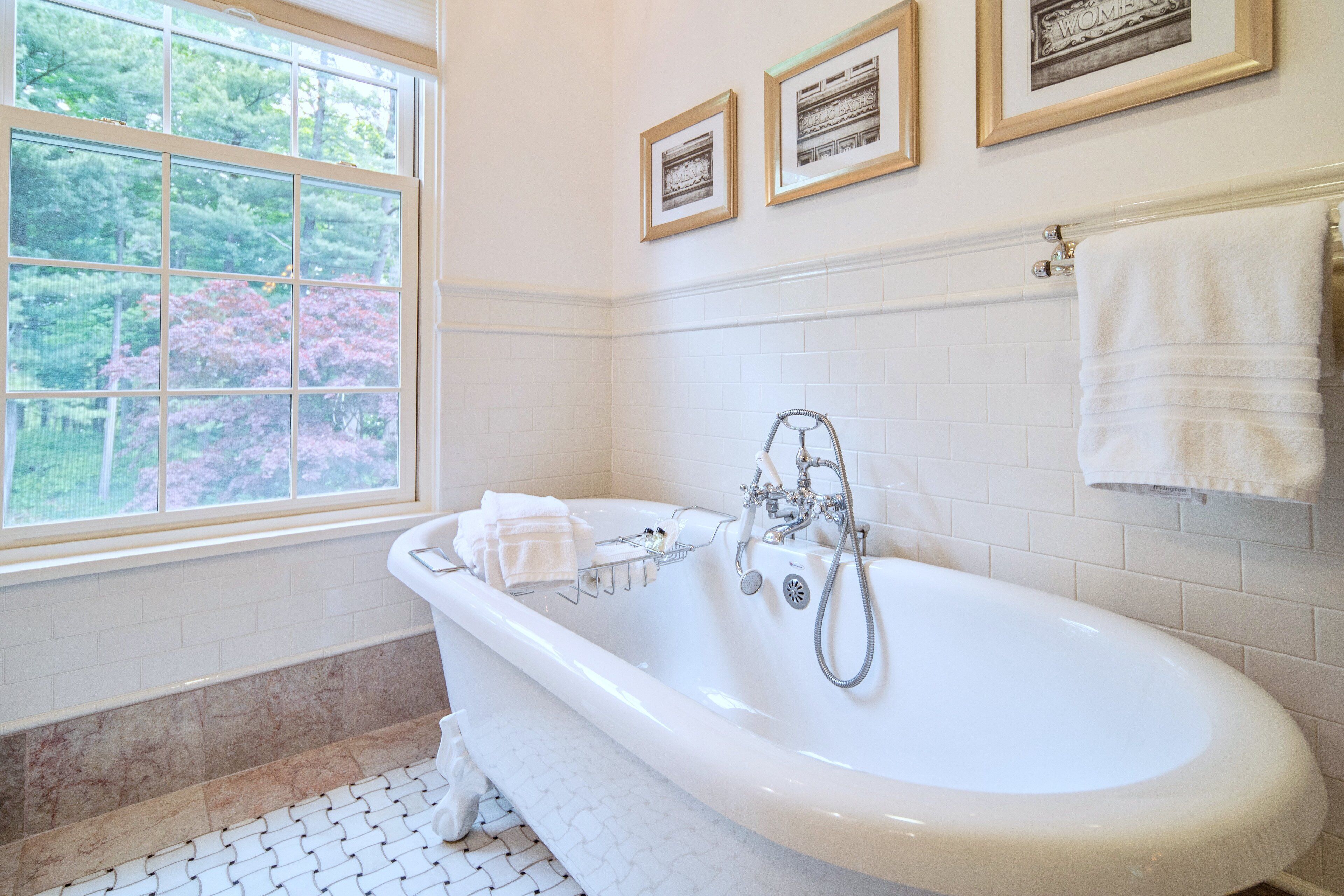 A bathroom with a freestanding bathtub, a window with a view of trees, and framed pictures on the wall.