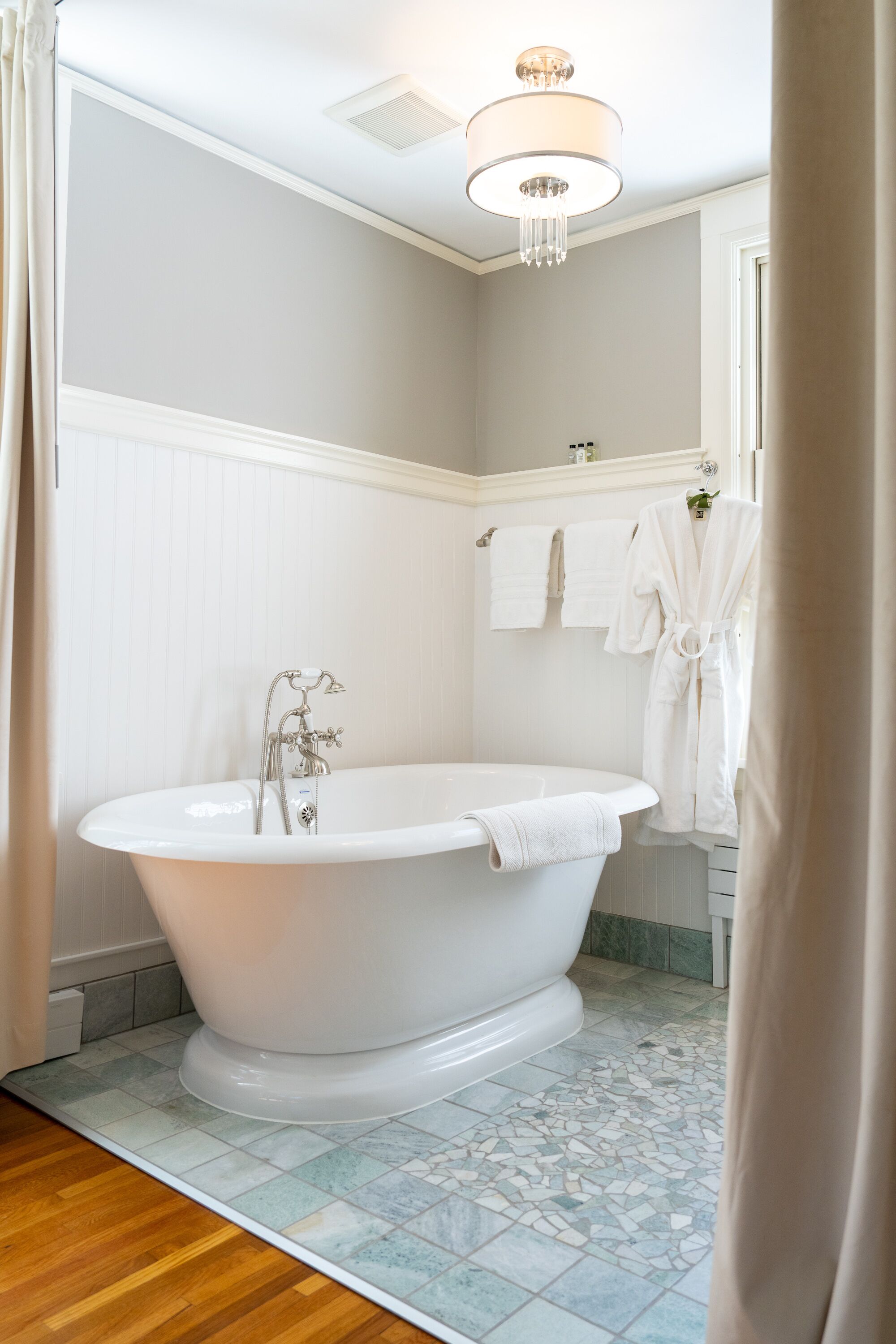 A bathroom with a freestanding bathtub, white towels, and a chandelier.