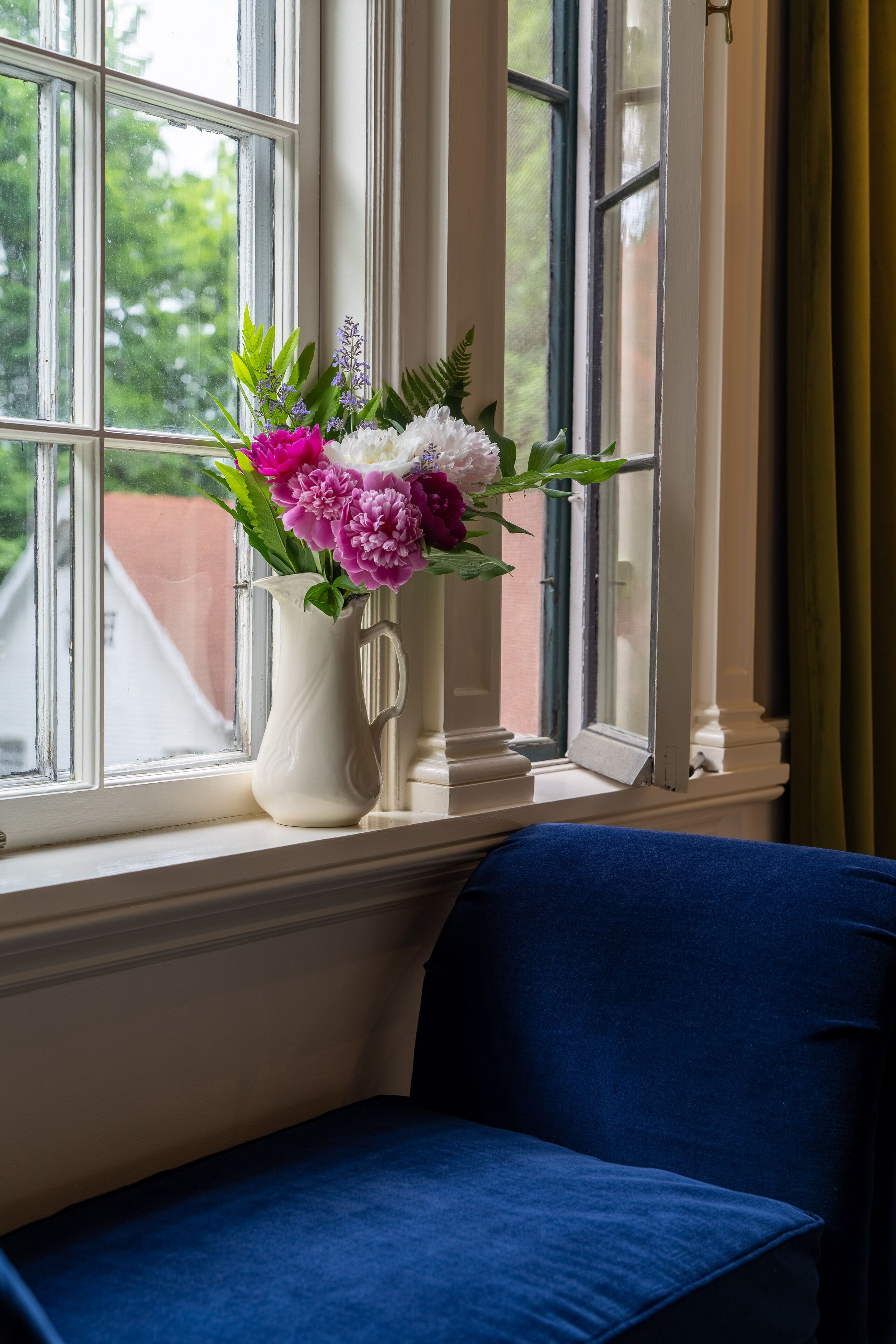 A white vase with flowers on a windowsill.