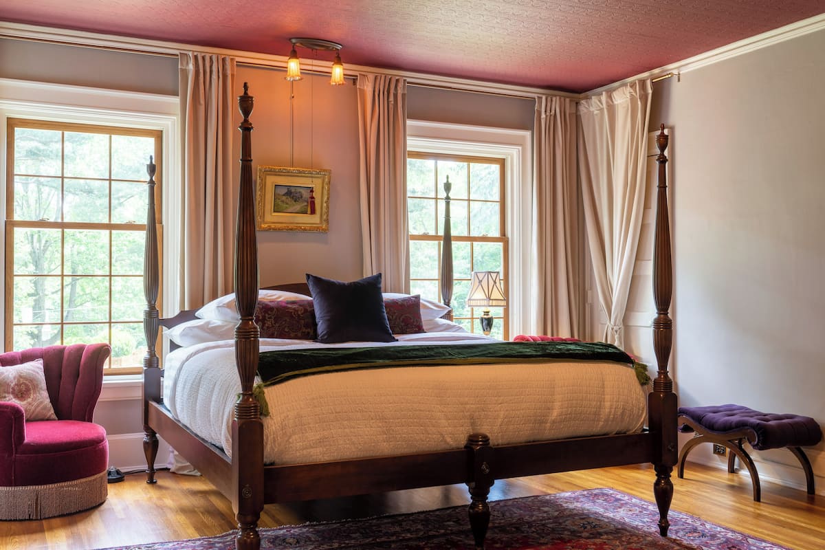 Un lit à baldaquin avec un plaid vert, un plancher en bois et un fauteuil rouge.