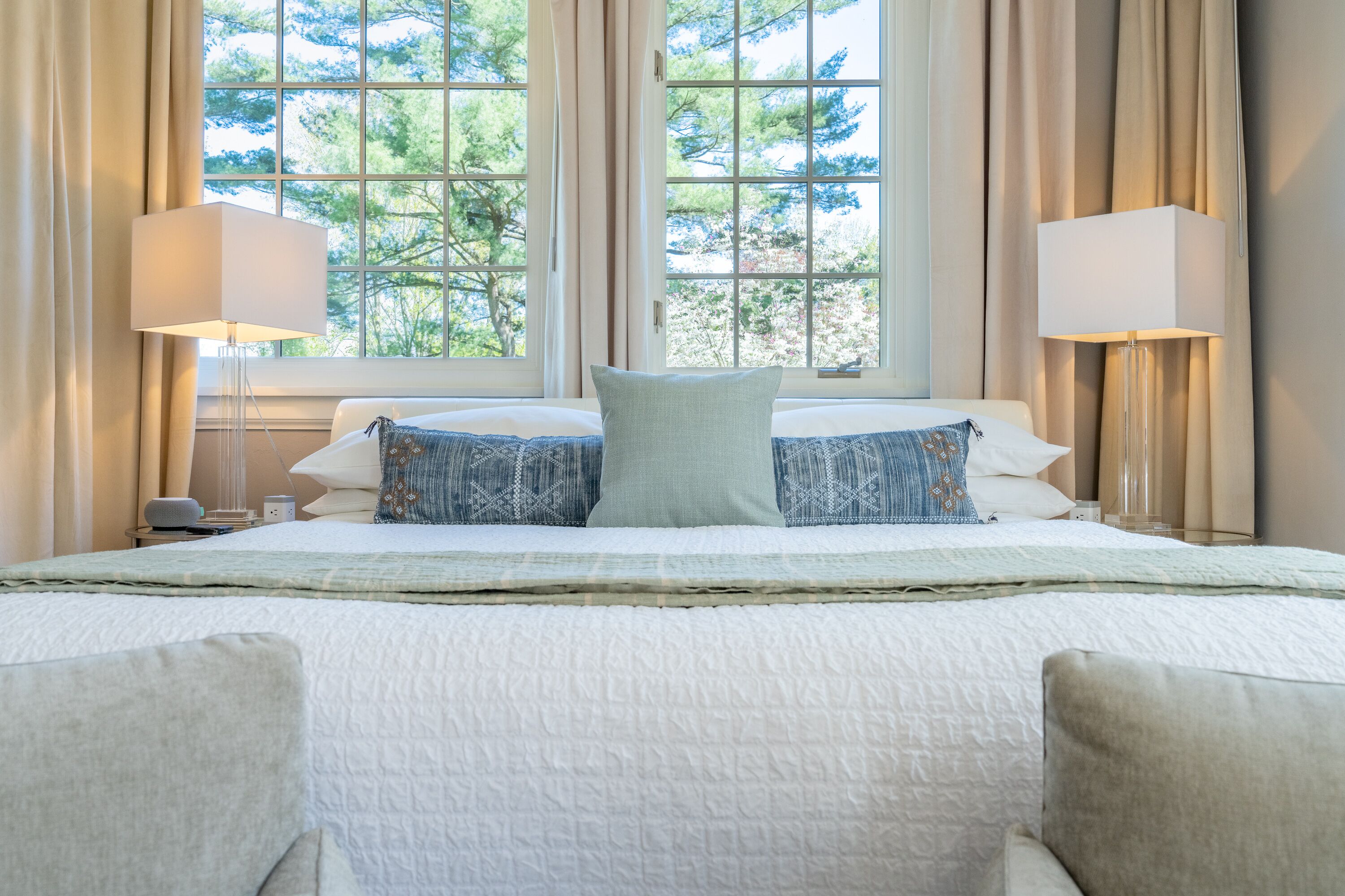 A hotel room with a large bed, two bedside lamps, and a view of trees through the window.