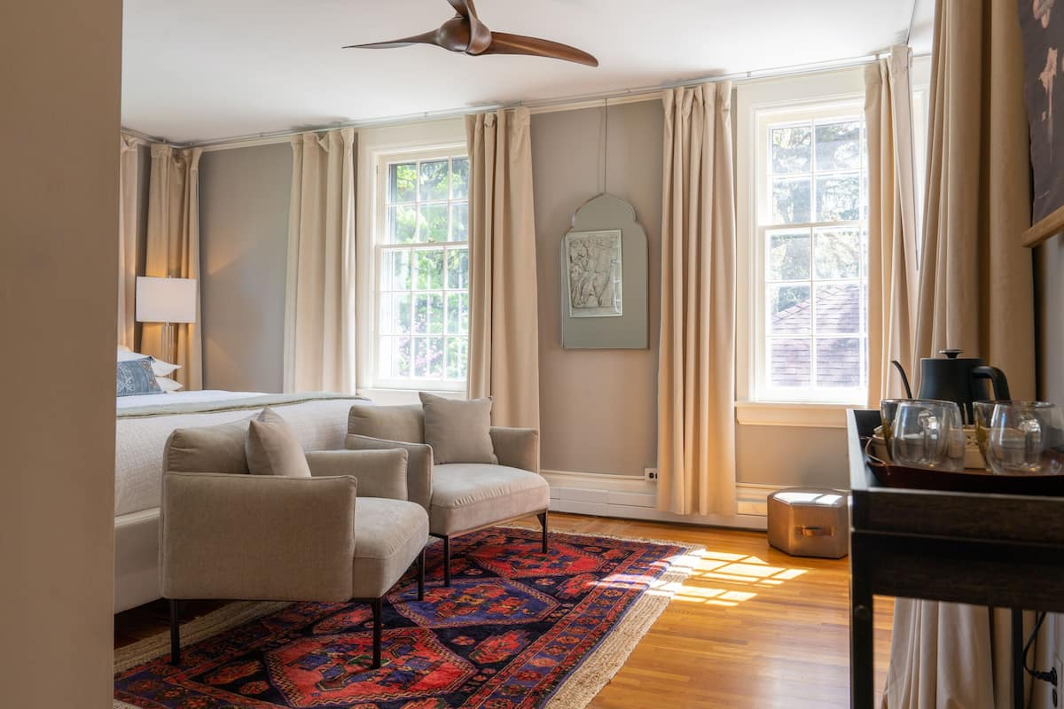Une chambre à coucher comprenant un lit, deux fauteuils, une table basse, un tapis et un ventilateur de plafond.