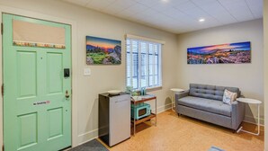 A room with a green door, a gray sofa, a small table, a microwave, and two paintings on the wall. - Blue Ridge Tourist Court (Boone)
