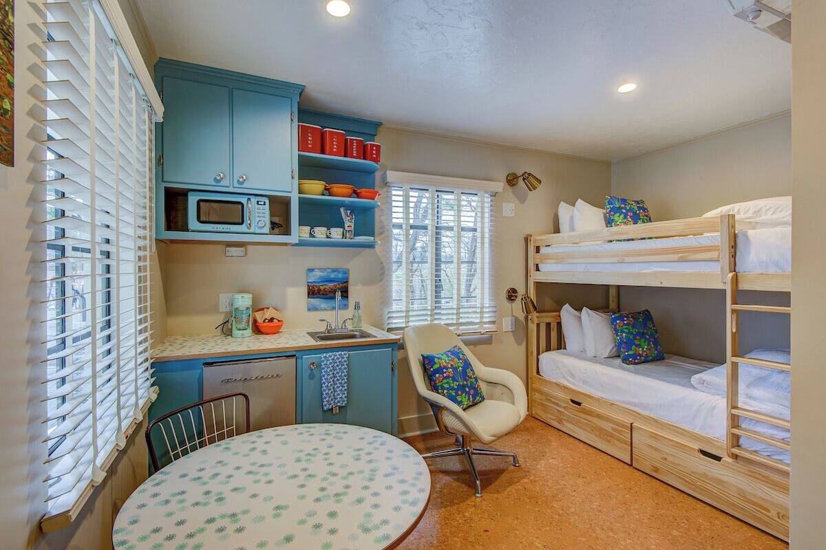 A compact room with a kitchenette, a dining table, a bunk bed, and a chair.