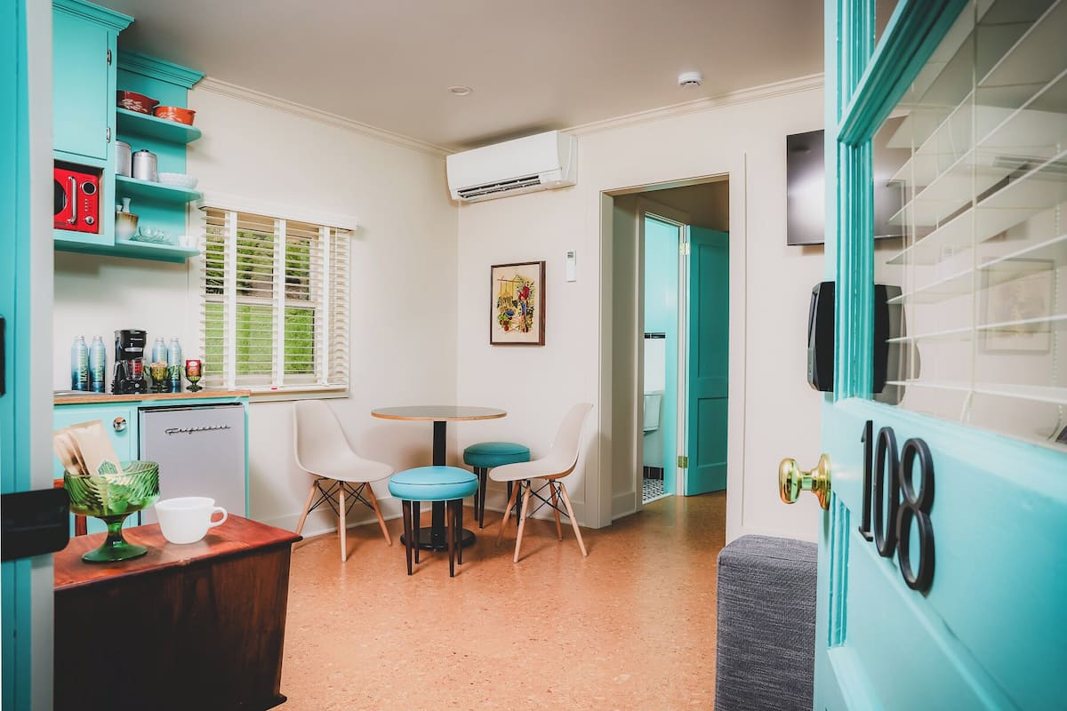 A compact kitchen with teal cabinetry, a coffee machine, and a refrigerator. There is a small dining area with two chairs and a table.