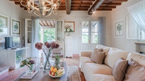 A cozy living room with a wooden ceiling, a white sofa, a coffee table with fruits and flowers, and a TV on a white cabinet. - 3 Bedrooms Farmhouse with Shared Pool in the Fattoria Sardi Wine Resort in Lucca (Monte San quirico)