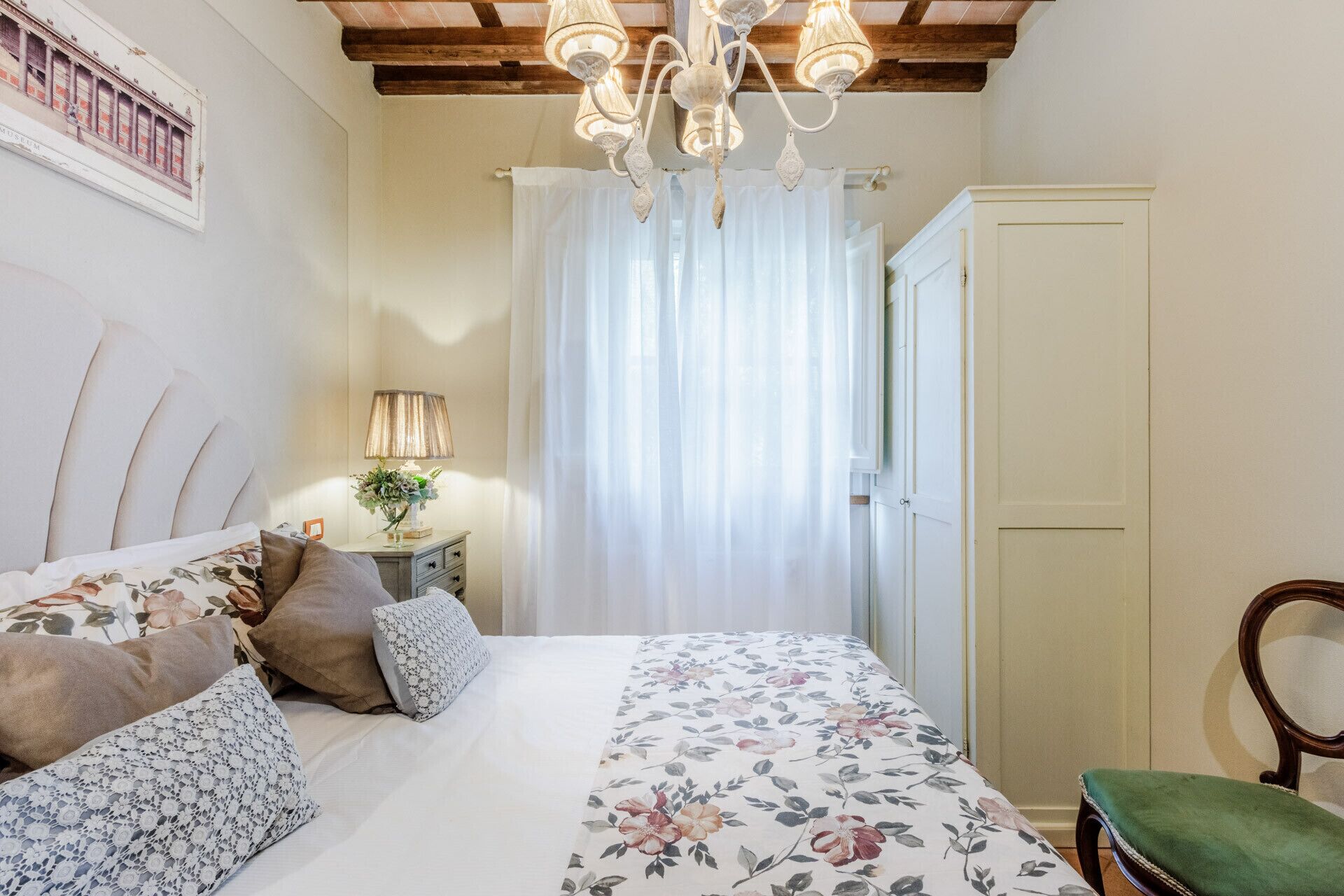 Een slaapkamer met een bed, nachtkastje, lamp, stoel en een deur.