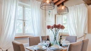 A dining table set for four with white plates, glasses, and cutlery, a vase with pink flowers, and two hanging light fixtures. - 3 Bedrooms Farmhouse with Shared Pool in the Fattoria Sardi Wine Resort in Lucca (Monte San quirico)