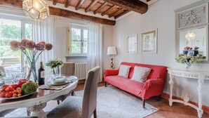 A cozy living room with a red sofa, a dining table with a vase of flowers, and a white console table with a mirror. - Donato one bedroom Farmhouse Apartment with shared Pool in Fattoria Sardi Wine Resort in Lucca (Monte San quirico)