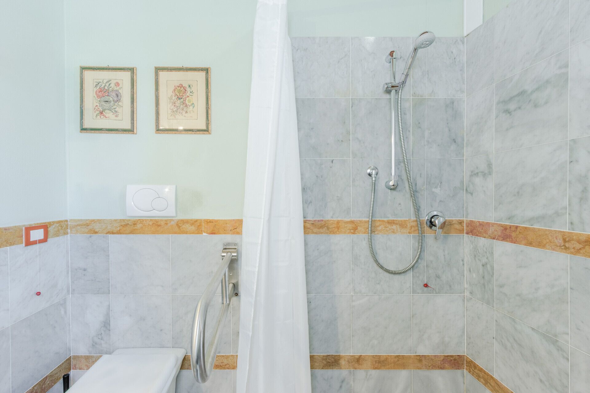 Une salle de bain avec une douche, des toilettes et deux tableaux représentant des motifs floraux, accrochés au mur.
