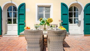 A patio with wicker chairs, a table with a vase of flowers, and a bottle of wine. - Elisa Farmhouse Apartment in Wine Resort in Lucca (Monte San quirico)