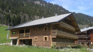 Una cabaña de madera con techo inclinado, varios balcones y vistas a una montaña boscosa.