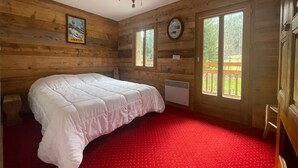 Un dormitorio de cabaña de madera con una cama, una alfombra roja, una ventana y una lámpara en el techo.