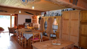 Un comedor rústico con muebles de madera, un televisor y una zona de cocina con armarios y estantes de madera.