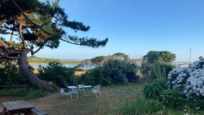 Un área de picnic con mesa y sillas de madera, rodeada de vegetación y vistas al mar.