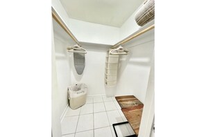 Bathroom features a minimalist design with a white tiled floor and walls, a wooden bench, and a laundry rack.